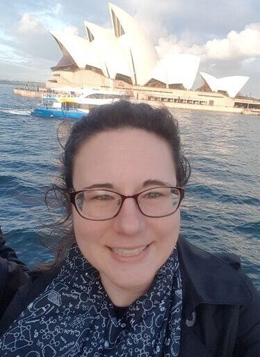 Professor Samantha Kristufek on a ferry in front of The Opera House, Sydney, Australia, wearing a scarf with chemistry symbols.